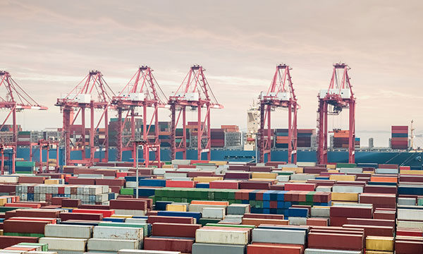 Shipping containers in container yard with container ship and cranes